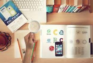 Étudiants en DUT Génie Biologie : Travaillez depuis chez vous! Image représentant plusieurs livres fermés et ouverts, sur un bureau sur lequel il y a également des crayons et un ordinateur ouvert. Quelqu'un tient une tasse dans sa main.
